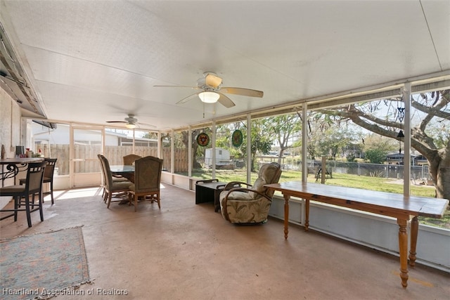 sunroom featuring ceiling fan and a water view