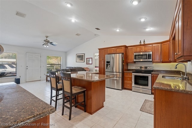 kitchen with sink, dark stone countertops, stainless steel appliances, a kitchen island, and vaulted ceiling