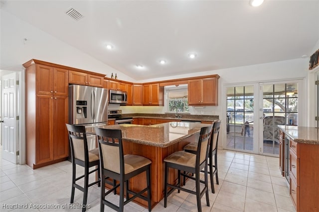 kitchen featuring a kitchen island, appliances with stainless steel finishes, lofted ceiling, dark stone countertops, and a kitchen breakfast bar