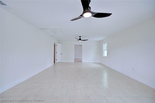 unfurnished room featuring attic access, ceiling fan, and baseboards