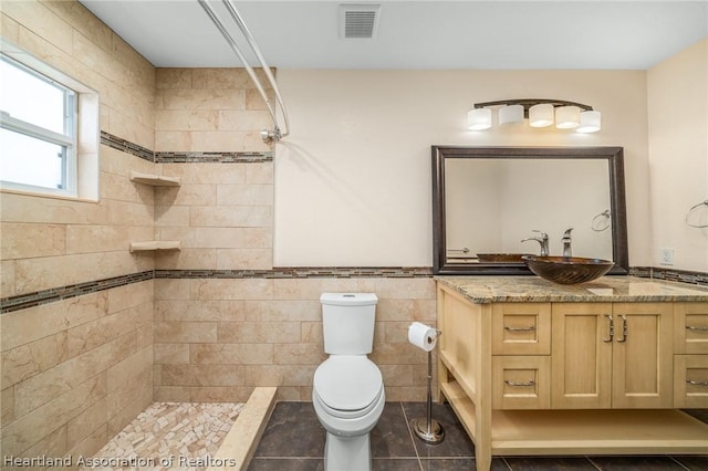 bathroom featuring a tile shower, tile patterned floors, toilet, vanity, and tile walls