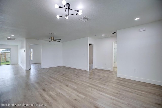 spare room featuring ceiling fan with notable chandelier, light hardwood / wood-style floors, and a textured ceiling