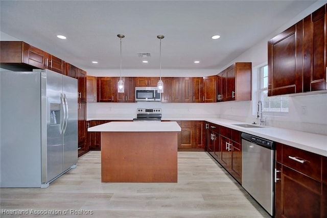 kitchen featuring light wood-type flooring, stainless steel appliances, sink, decorative light fixtures, and a center island