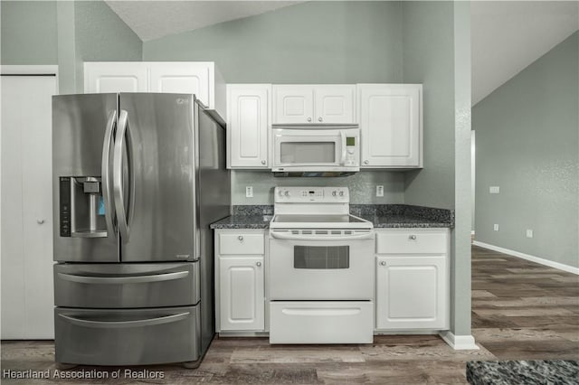 kitchen featuring white appliances, vaulted ceiling, dark wood-type flooring, dark stone countertops, and white cabinets