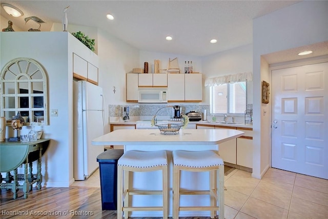 kitchen with white appliances, a kitchen island, a sink, light countertops, and backsplash