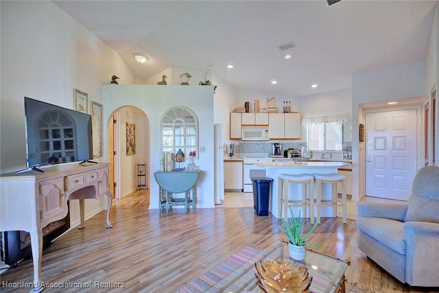 living room with visible vents, recessed lighting, arched walkways, light wood-style floors, and vaulted ceiling