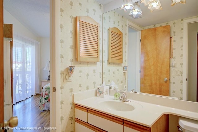 ensuite bathroom with connected bathroom, wallpapered walls, a chandelier, wood finished floors, and vanity