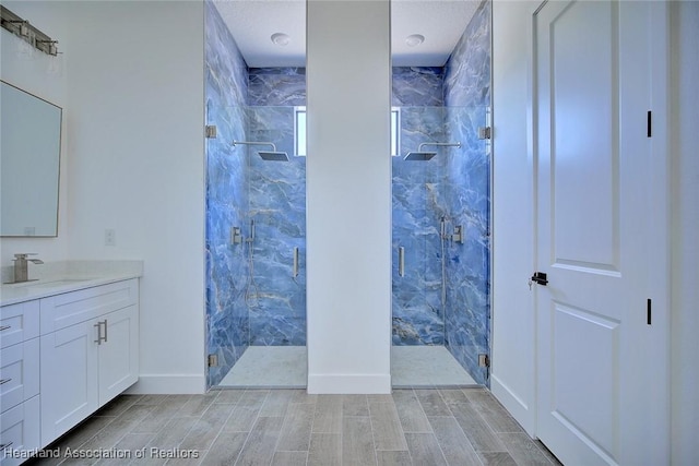 full bath featuring vanity, wood finish floors, baseboards, and a marble finish shower