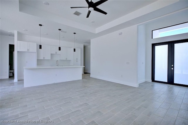 unfurnished living room featuring a sink, a raised ceiling, a ceiling fan, visible vents, and french doors