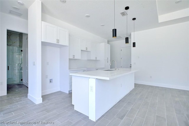 kitchen with white cabinetry, a sink, visible vents, baseboards, and an island with sink