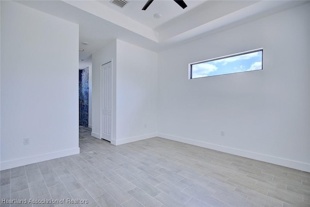 spare room featuring a raised ceiling, a ceiling fan, visible vents, light wood-style flooring, and baseboards