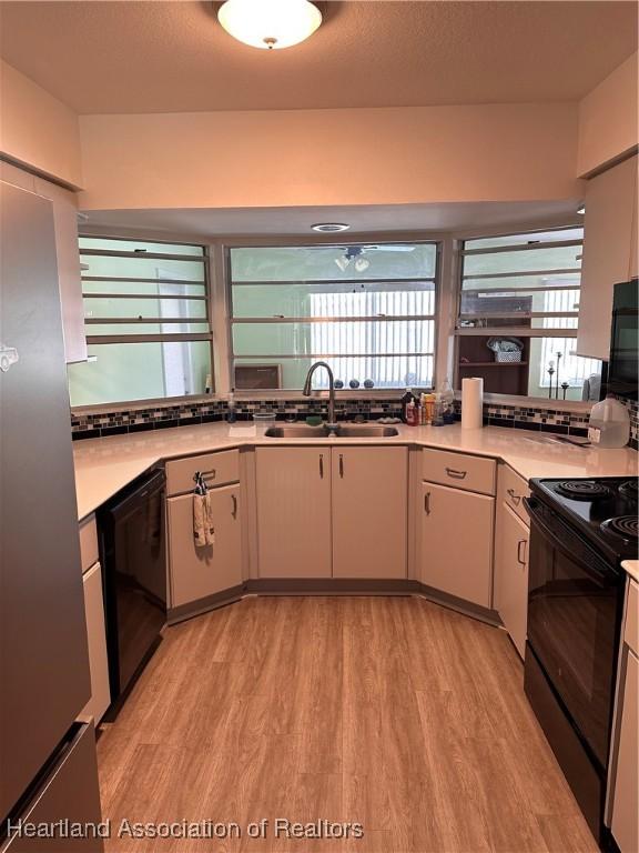 kitchen with a healthy amount of sunlight, light wood-type flooring, black appliances, and sink