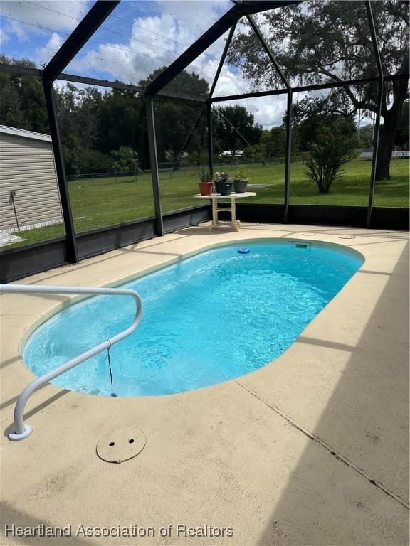 view of swimming pool featuring a lawn, glass enclosure, and a patio area