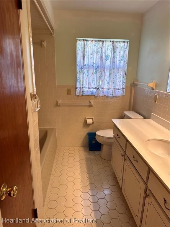 bathroom featuring a tub, tile patterned floors, toilet, vanity, and tile walls