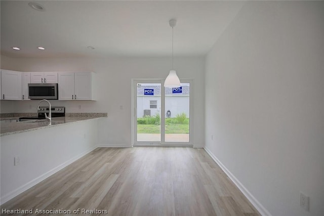 kitchen with light stone countertops, appliances with stainless steel finishes, light wood-type flooring, pendant lighting, and white cabinets