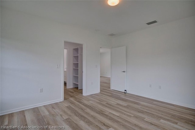 unfurnished bedroom with light wood-type flooring, a spacious closet, and a closet