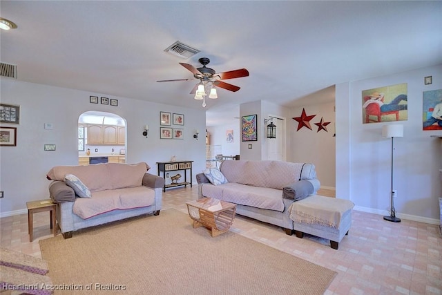 living area featuring arched walkways, ceiling fan, visible vents, and baseboards