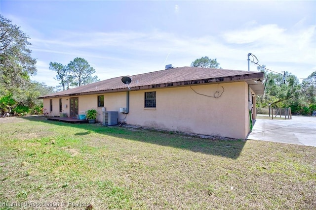 rear view of property featuring a lawn, stucco siding, and central air condition unit