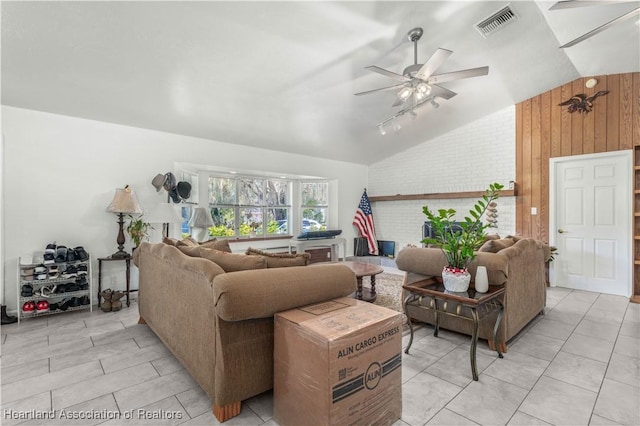 living room with vaulted ceiling, brick wall, wood walls, rail lighting, and ceiling fan