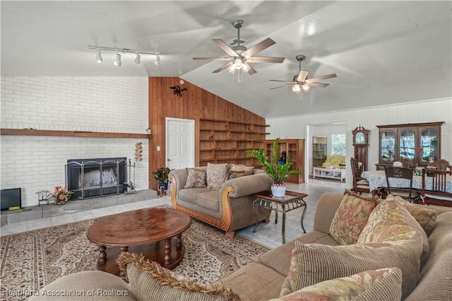 tiled living room featuring ceiling fan, a fireplace, vaulted ceiling, and wood walls