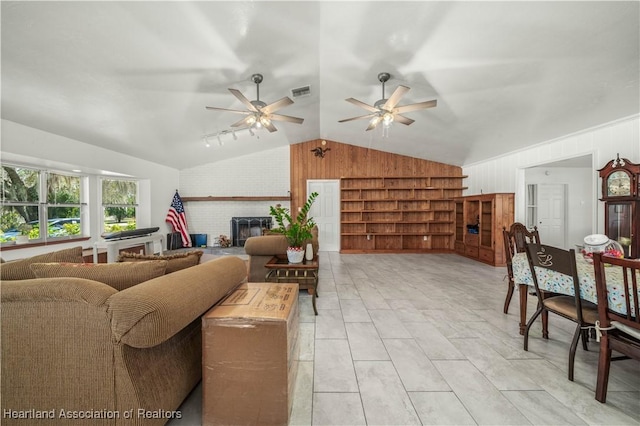 living room featuring ceiling fan, lofted ceiling, a fireplace, and wood walls