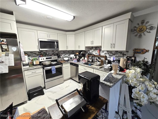 kitchen featuring white cabinetry, light stone counters, a textured ceiling, stainless steel appliances, and backsplash