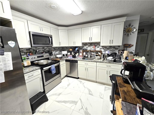 kitchen featuring appliances with stainless steel finishes, tasteful backsplash, white cabinets, light stone counters, and a textured ceiling