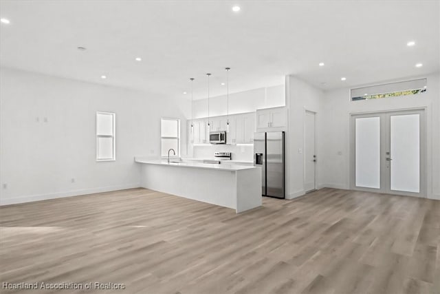 kitchen with appliances with stainless steel finishes, light hardwood / wood-style floors, kitchen peninsula, pendant lighting, and white cabinetry