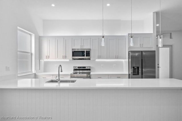 kitchen featuring kitchen peninsula, pendant lighting, white cabinets, appliances with stainless steel finishes, and sink