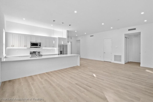 kitchen featuring hanging light fixtures, light wood-type flooring, white cabinetry, appliances with stainless steel finishes, and sink