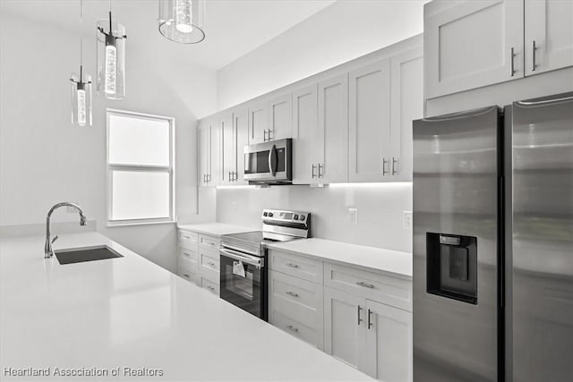 kitchen with stainless steel appliances, white cabinetry, sink, and hanging light fixtures