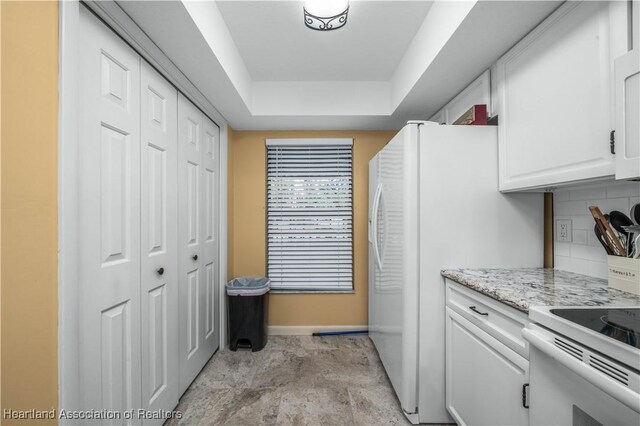 kitchen featuring tasteful backsplash, light stone counters, a raised ceiling, electric stove, and white cabinets