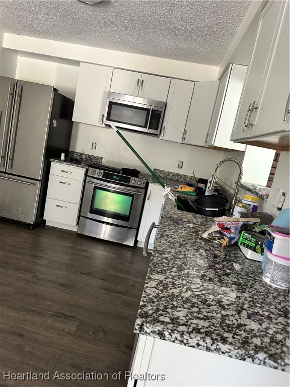 kitchen featuring stainless steel appliances, dark wood-style floors, a textured ceiling, dark stone countertops, and white cabinetry