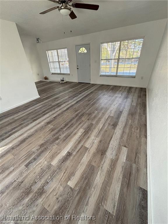 unfurnished living room with baseboards, ceiling fan, plenty of natural light, and wood finished floors
