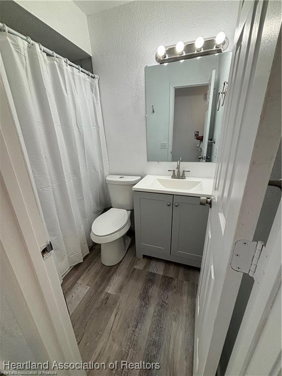 full bath featuring toilet, wood finished floors, a shower with curtain, a textured wall, and vanity