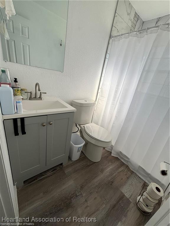 full bathroom with toilet, curtained shower, vanity, wood finished floors, and a textured wall