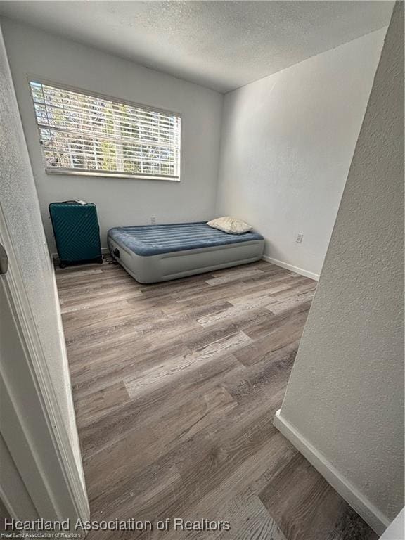 bedroom featuring a textured ceiling, a textured wall, and wood finished floors