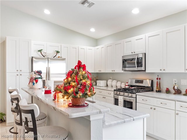 kitchen featuring white cabinets, a kitchen breakfast bar, vaulted ceiling, light stone countertops, and appliances with stainless steel finishes