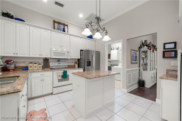 kitchen with white cabinetry, a center island, hanging light fixtures, white appliances, and ornamental molding