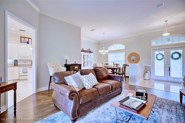 living area with french doors, crown molding, visible vents, light wood-style flooring, and a chandelier