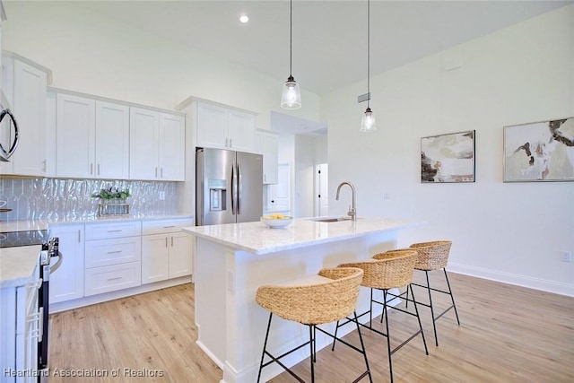 kitchen with stainless steel fridge with ice dispenser, hanging light fixtures, white cabinets, backsplash, and a center island with sink