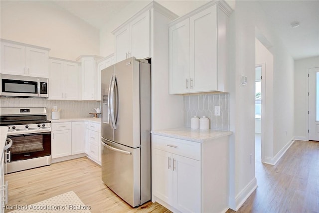 kitchen featuring white cabinets, light wood-type flooring, backsplash, stainless steel appliances, and light stone counters