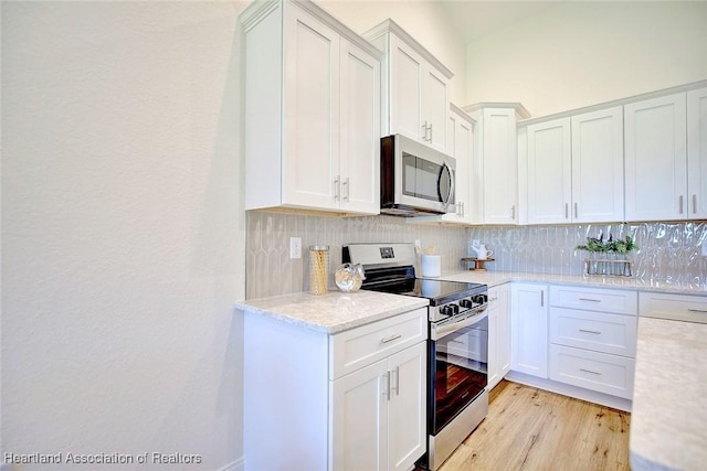 kitchen with white cabinets, appliances with stainless steel finishes, light hardwood / wood-style flooring, and tasteful backsplash