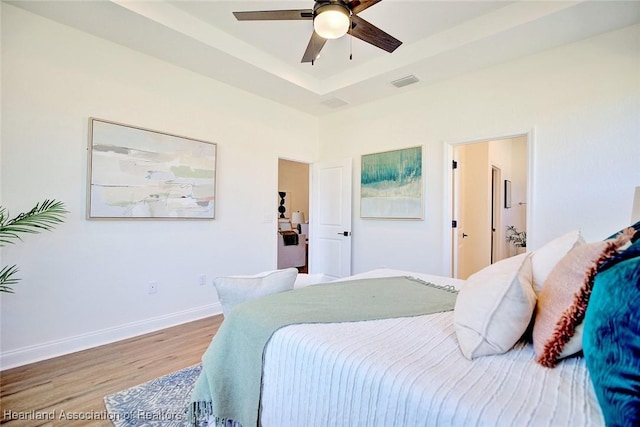 bedroom with light wood-type flooring, ceiling fan, and a tray ceiling