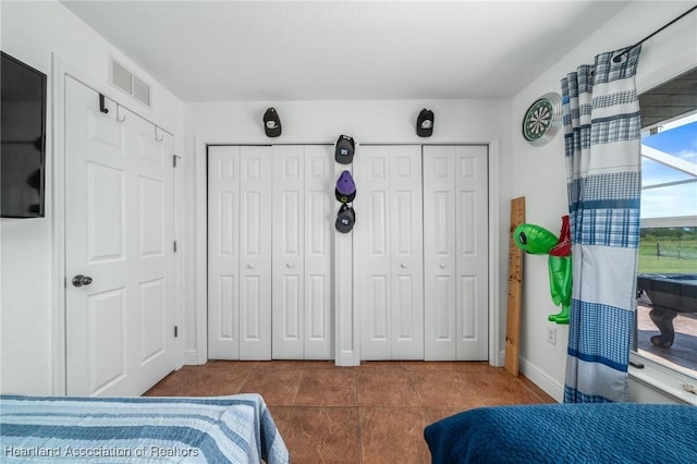 bedroom with baseboards, two closets, visible vents, and tile patterned floors