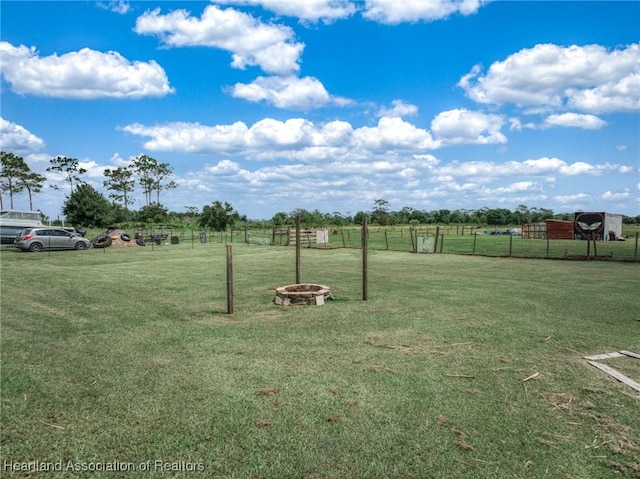 view of yard featuring an outdoor fire pit, a rural view, and fence