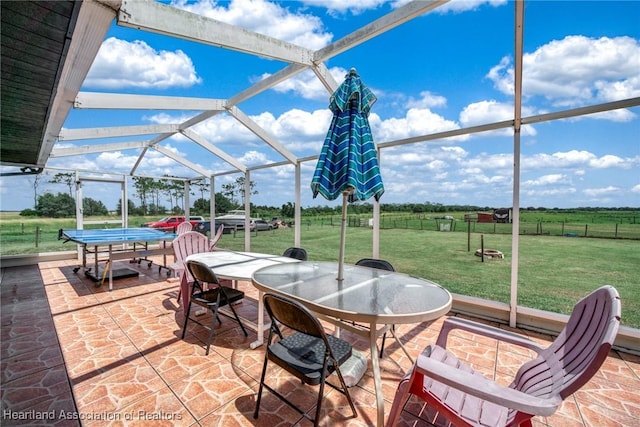 view of patio featuring glass enclosure, outdoor dining space, and a rural view