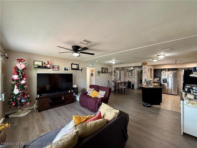 living room featuring hardwood / wood-style flooring, ceiling fan, and a textured ceiling