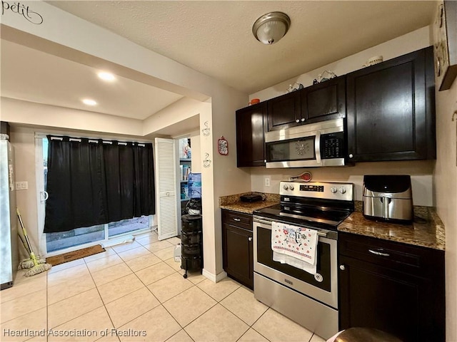 kitchen featuring appliances with stainless steel finishes, light tile patterned floors, and dark stone countertops