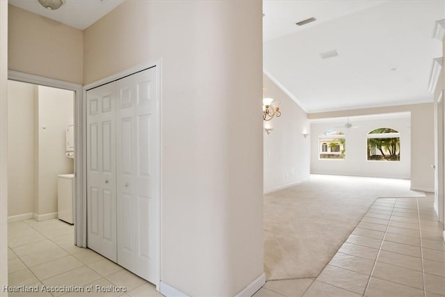 corridor featuring light carpet, crown molding, and an inviting chandelier